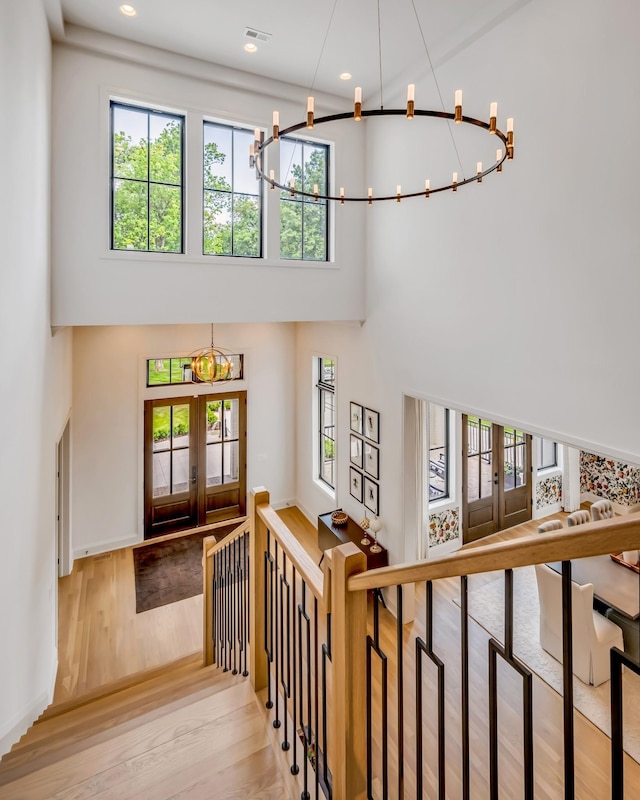 staircase with a high ceiling, hardwood / wood-style floors, french doors, and a notable chandelier