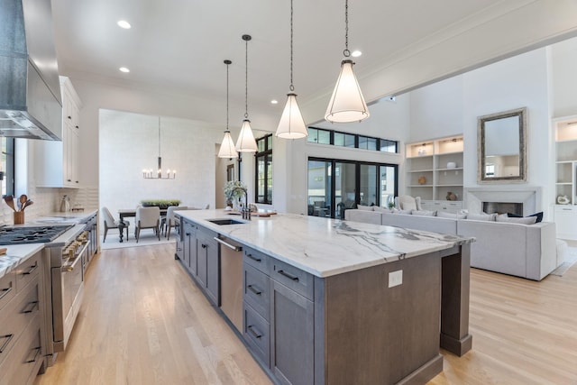 kitchen with pendant lighting, wall chimney exhaust hood, white cabinetry, sink, and a large island