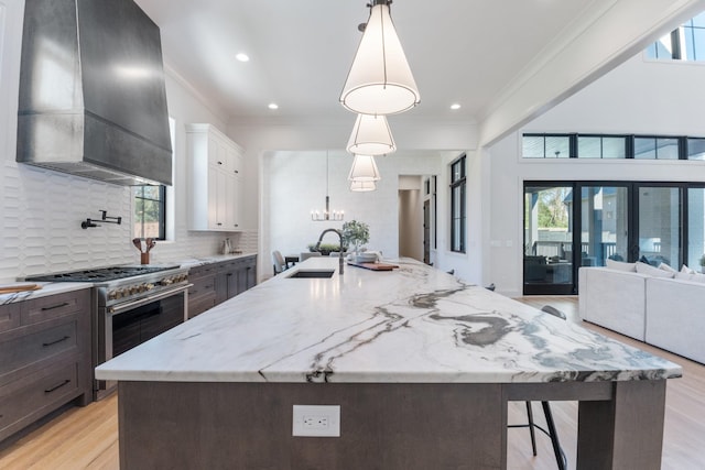 kitchen featuring decorative light fixtures, wall chimney range hood, sink, range with two ovens, and white cabinets