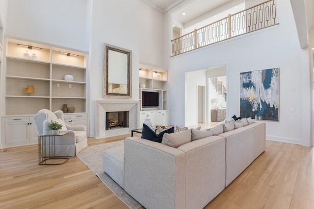 living room with light wood-type flooring, a premium fireplace, a high ceiling, and built in shelves