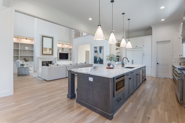 kitchen with a center island with sink, stainless steel appliances, built in features, white cabinets, and sink