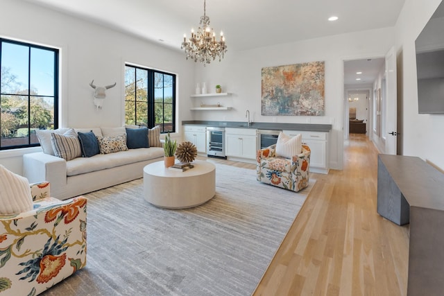 living room featuring light wood-type flooring, an inviting chandelier, beverage cooler, and sink