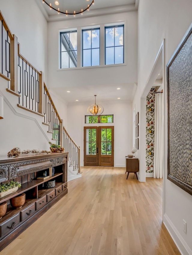 foyer entrance with light hardwood / wood-style floors, french doors, a towering ceiling, and an inviting chandelier