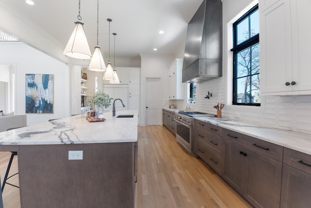 kitchen with white cabinetry, wall chimney range hood, high end stove, and tasteful backsplash