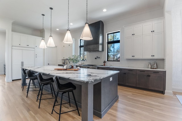 kitchen featuring a large island, white cabinetry, wall chimney exhaust hood, and hanging light fixtures