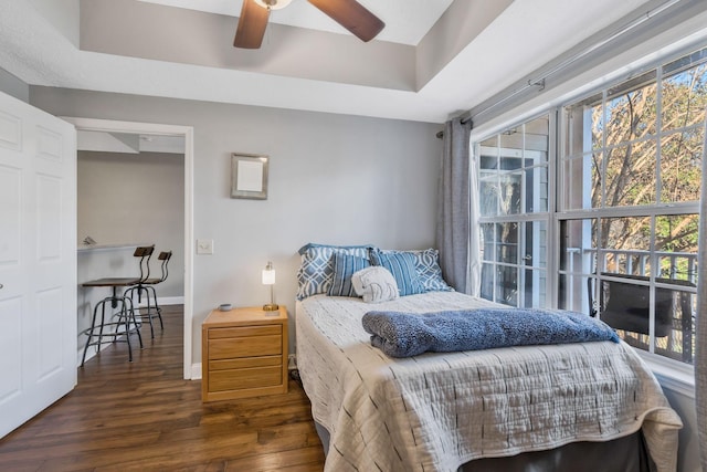 bedroom with ceiling fan, dark hardwood / wood-style flooring, and a tray ceiling