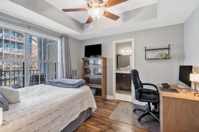 bedroom with ceiling fan, connected bathroom, dark hardwood / wood-style flooring, and a raised ceiling