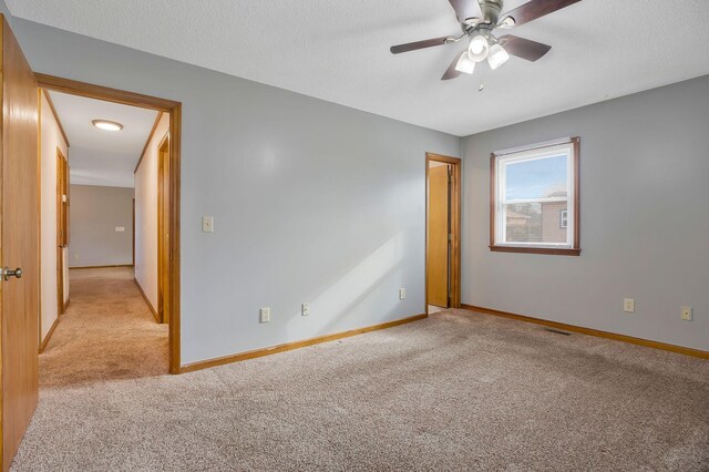 empty room featuring ceiling fan, light carpet, and a textured ceiling