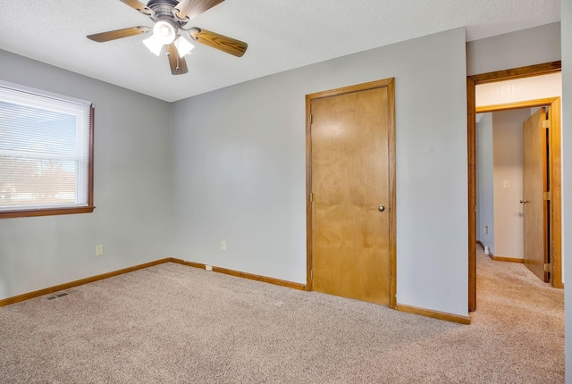 unfurnished bedroom with ceiling fan, light colored carpet, and a textured ceiling