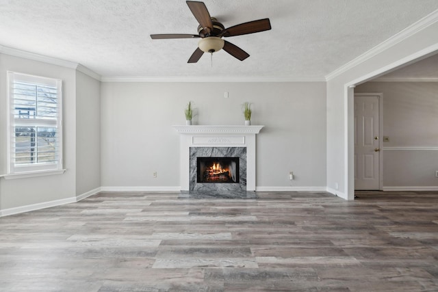 unfurnished living room featuring ceiling fan, a premium fireplace, crown molding, and hardwood / wood-style flooring