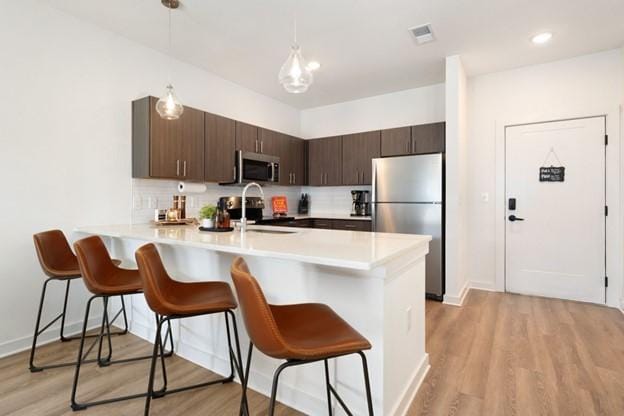 kitchen featuring dark brown cabinetry, appliances with stainless steel finishes, a kitchen bar, kitchen peninsula, and light wood-type flooring