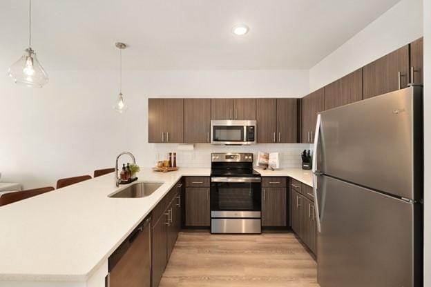 kitchen featuring decorative light fixtures, kitchen peninsula, sink, appliances with stainless steel finishes, and dark brown cabinets