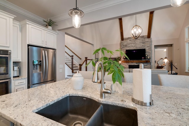 kitchen with stainless steel appliances, pendant lighting, light stone counters, and sink