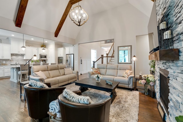 living room featuring a notable chandelier, dark hardwood / wood-style floors, beam ceiling, a stone fireplace, and high vaulted ceiling