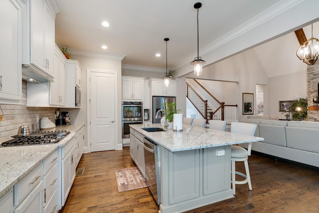 kitchen with stainless steel appliances, decorative backsplash, white cabinets, and a center island with sink