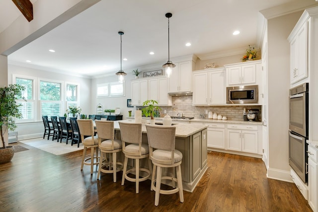 kitchen with hanging light fixtures, white cabinets, stainless steel appliances, and an island with sink