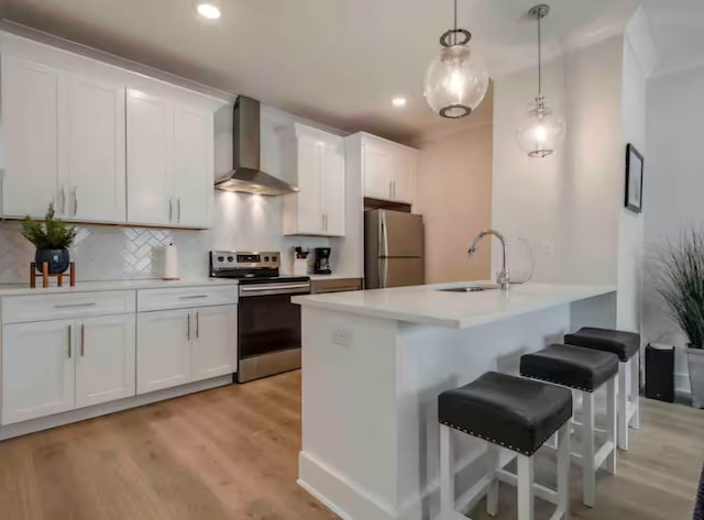 kitchen with decorative light fixtures, white cabinets, wall chimney exhaust hood, and stainless steel appliances