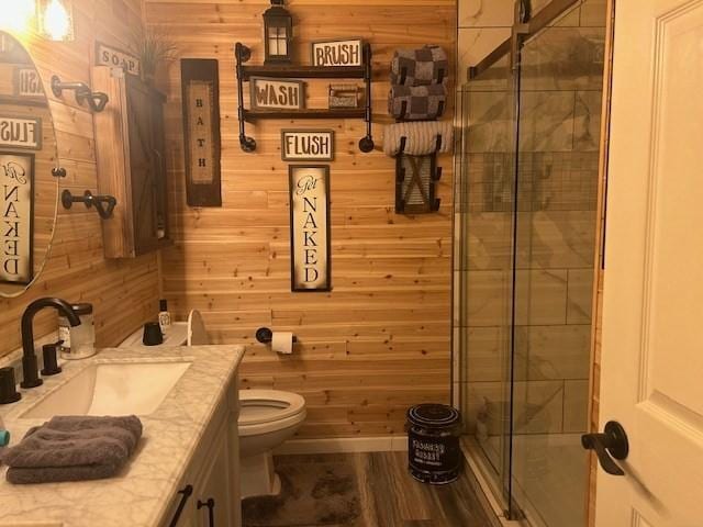 bathroom with toilet, vanity, a shower with door, and wood walls