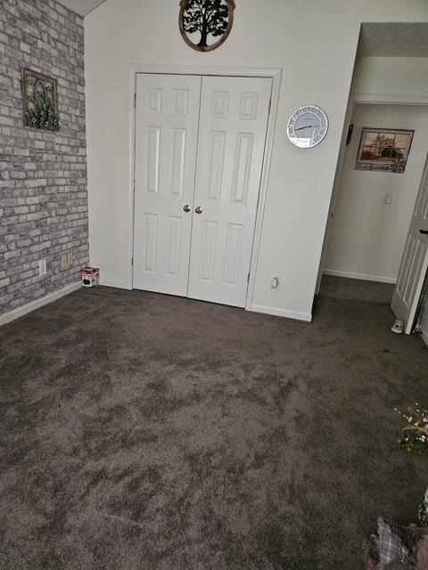 unfurnished bedroom with dark colored carpet and brick wall