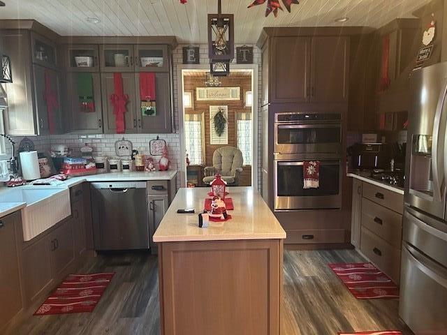 kitchen with dark hardwood / wood-style floors, pendant lighting, a center island, decorative backsplash, and stainless steel appliances