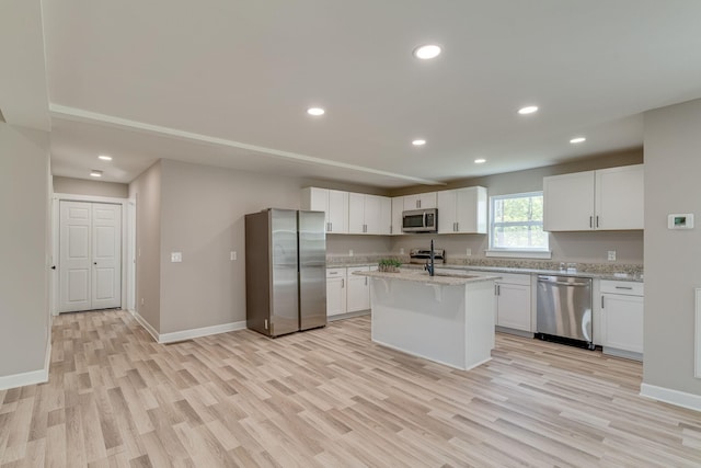 kitchen featuring light stone counters, white cabinetry, stainless steel appliances, and an island with sink