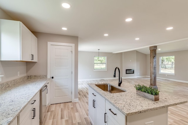 kitchen featuring light stone countertops, white cabinets, light hardwood / wood-style floors, sink, and a kitchen island with sink