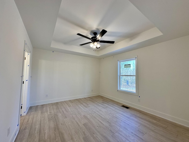 spare room with ceiling fan, a tray ceiling, and light hardwood / wood-style floors