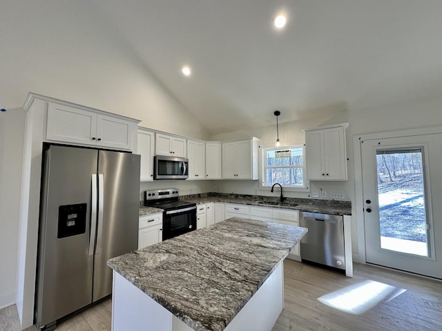 kitchen with stainless steel appliances, dark stone counters, a kitchen island, white cabinets, and sink