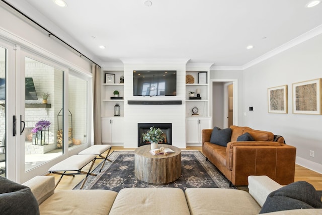 living room with wood-type flooring, a large fireplace, and ornamental molding