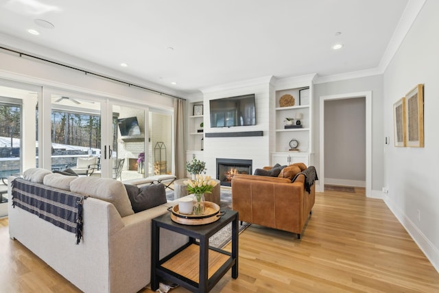 living room with built in features, light hardwood / wood-style flooring, crown molding, and a fireplace