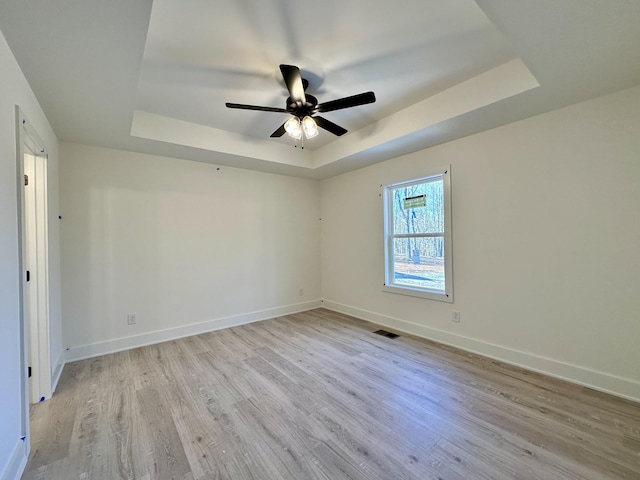 spare room with ceiling fan, light hardwood / wood-style floors, and a tray ceiling