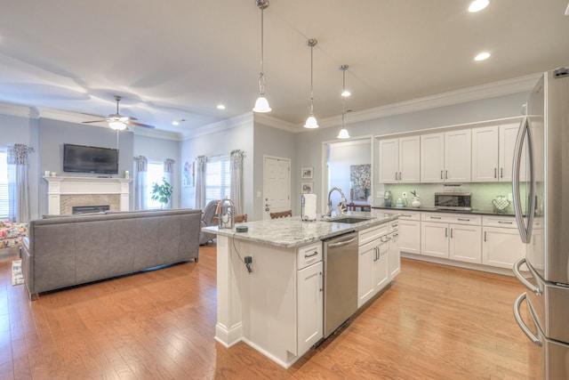 kitchen featuring white cabinets, appliances with stainless steel finishes, decorative light fixtures, an island with sink, and sink