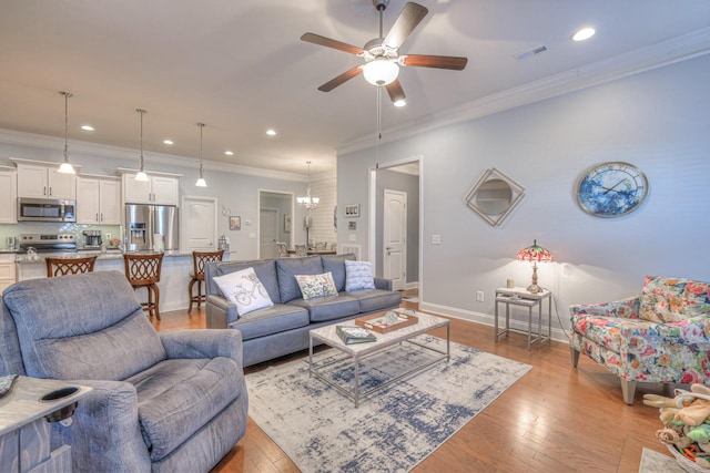 living room with ceiling fan with notable chandelier, light hardwood / wood-style flooring, and ornamental molding