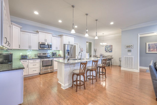 kitchen featuring decorative light fixtures, tasteful backsplash, a center island with sink, stainless steel appliances, and white cabinets