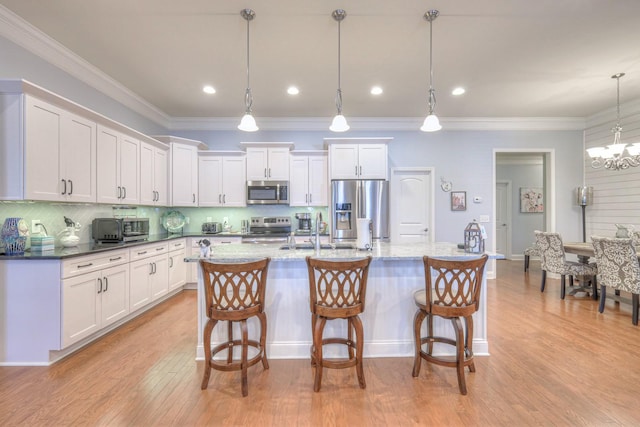 kitchen featuring stainless steel appliances, an island with sink, white cabinetry, and decorative light fixtures