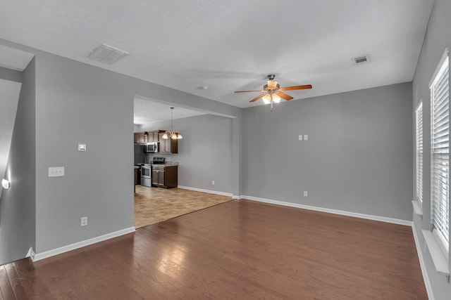 unfurnished living room with ceiling fan with notable chandelier and dark hardwood / wood-style floors