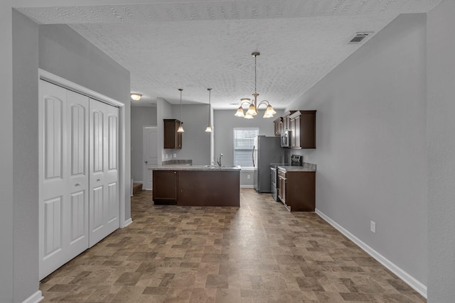 kitchen with a textured ceiling, pendant lighting, appliances with stainless steel finishes, a kitchen island, and dark brown cabinets