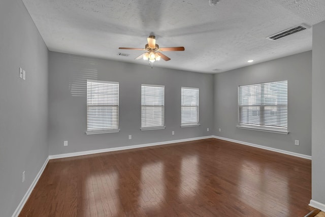 empty room featuring dark wood-type flooring, a textured ceiling, and a healthy amount of sunlight