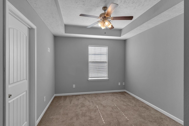 unfurnished room featuring a textured ceiling, light carpet, and a tray ceiling