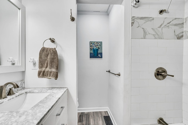 bathroom featuring wood-type flooring, crown molding, vanity, and a tile shower