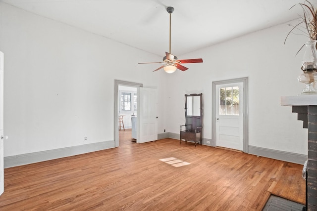 unfurnished living room featuring light hardwood / wood-style floors, a brick fireplace, ceiling fan, and vaulted ceiling