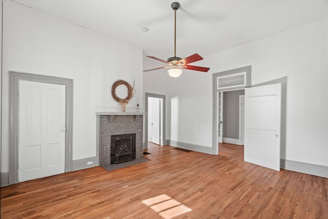 unfurnished living room with ceiling fan, a wood stove, and hardwood / wood-style floors