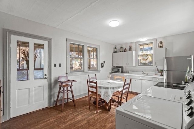 kitchen with appliances with stainless steel finishes, dark hardwood / wood-style floors, white cabinets, washer / clothes dryer, and sink