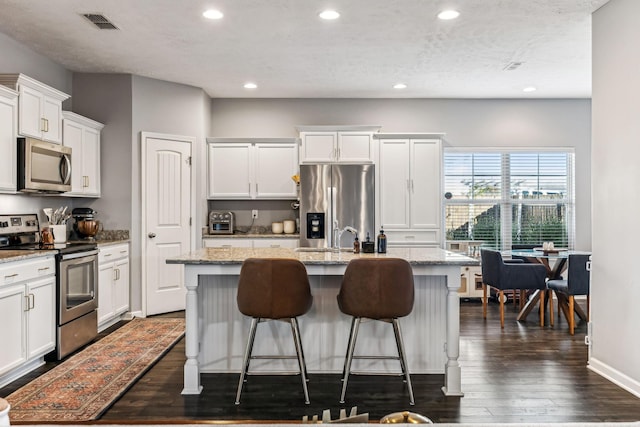 kitchen featuring light stone countertops, appliances with stainless steel finishes, an island with sink, and white cabinetry