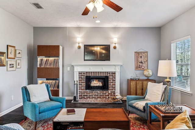 living room featuring ceiling fan, a fireplace, a textured ceiling, and dark hardwood / wood-style floors