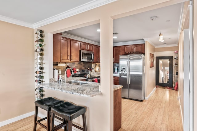 kitchen with stainless steel appliances, light hardwood / wood-style floors, kitchen peninsula, light stone counters, and a breakfast bar