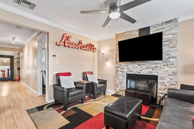 living room with ceiling fan, wood-type flooring, ornamental molding, and a stone fireplace