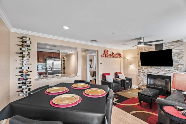 interior space featuring light wood-type flooring, ceiling fan, crown molding, and a fireplace