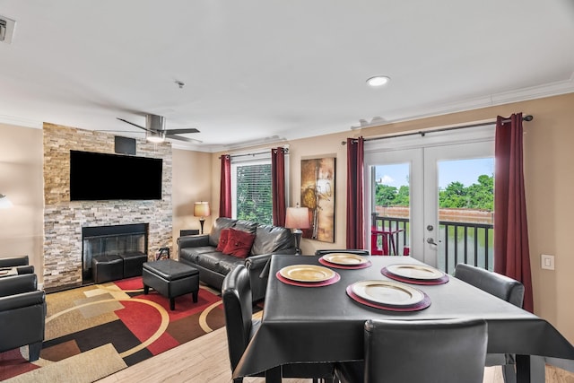 dining area featuring ceiling fan, french doors, a stone fireplace, and ornamental molding