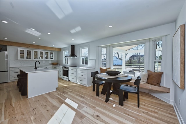 kitchen featuring white cabinetry, a kitchen island with sink, stainless steel electric range, refrigerator, and wall chimney range hood